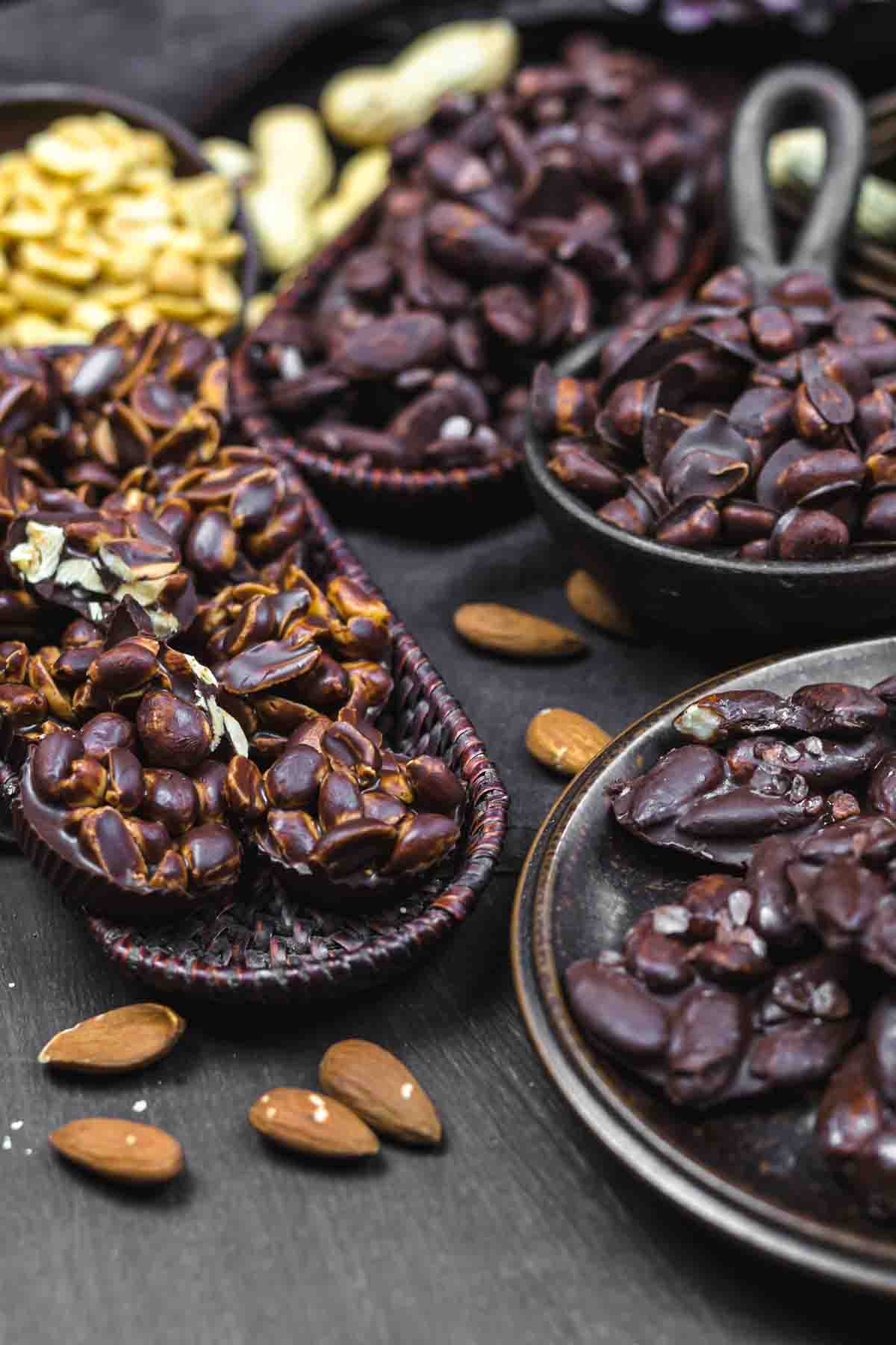 Variety of chocolate-covered nuts and almonds placed in different bowls on a dark background.