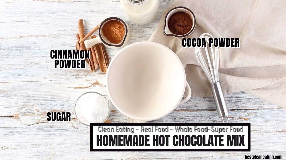 An empty bowl surrounded by cinnamon powder, cocoa powder, sugar, milk, and a whisk on a wooden surface. Text reads: "Homemade Hot Chocolate Mix.