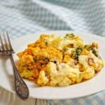 A plate of baked broccoli and cauliflower casserole with a breadcrumb topping, served with a fork on a white plate.