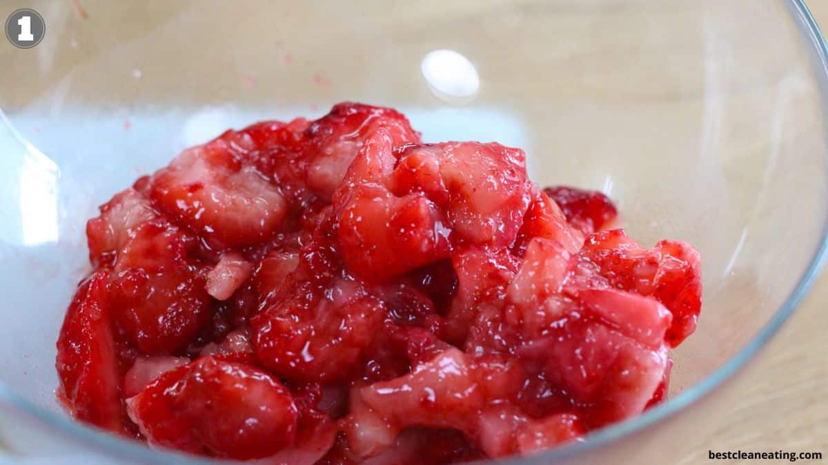 Chopped strawberries mixed with sugar in a clear glass bowl.