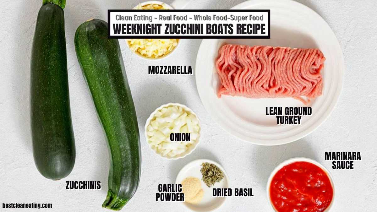 Two zucchinis, mozzarella, lean ground turkey, onion, garlic powder, dried basil, and marinara sauce are displayed on a white surface, labeled as ingredients for zucchini boats.