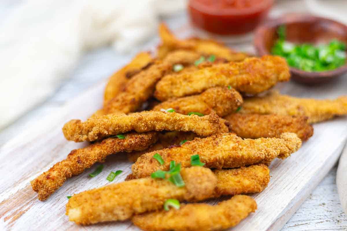 Crispy chicken strips served with sauce and garnish.