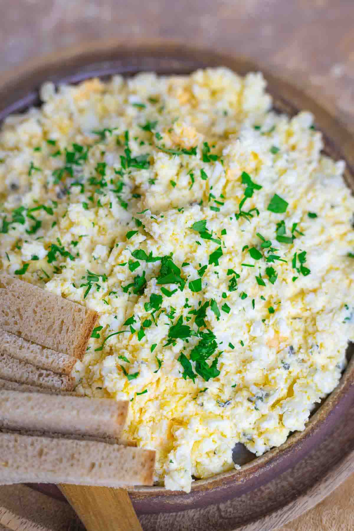 A plate of scrambled eggs topped with chopped fresh herbs, served with slices of brown bread on the side.