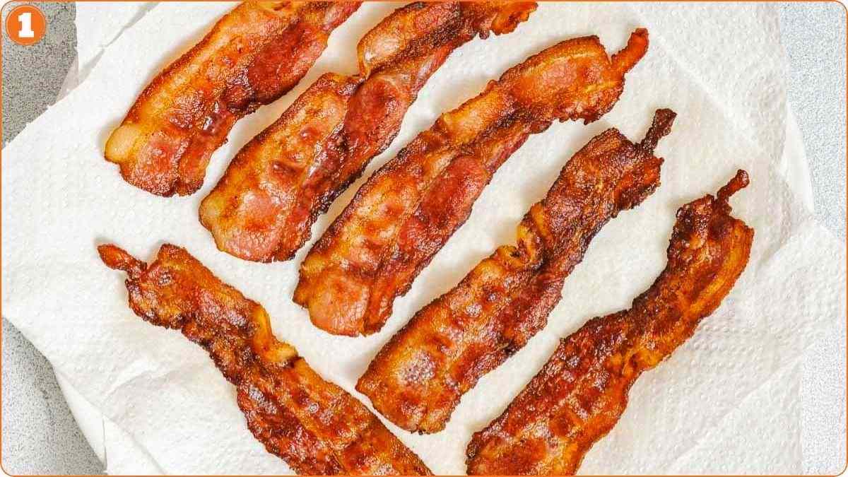 Six strips of cooked bacon are placed on a paper towel to drain excess grease.