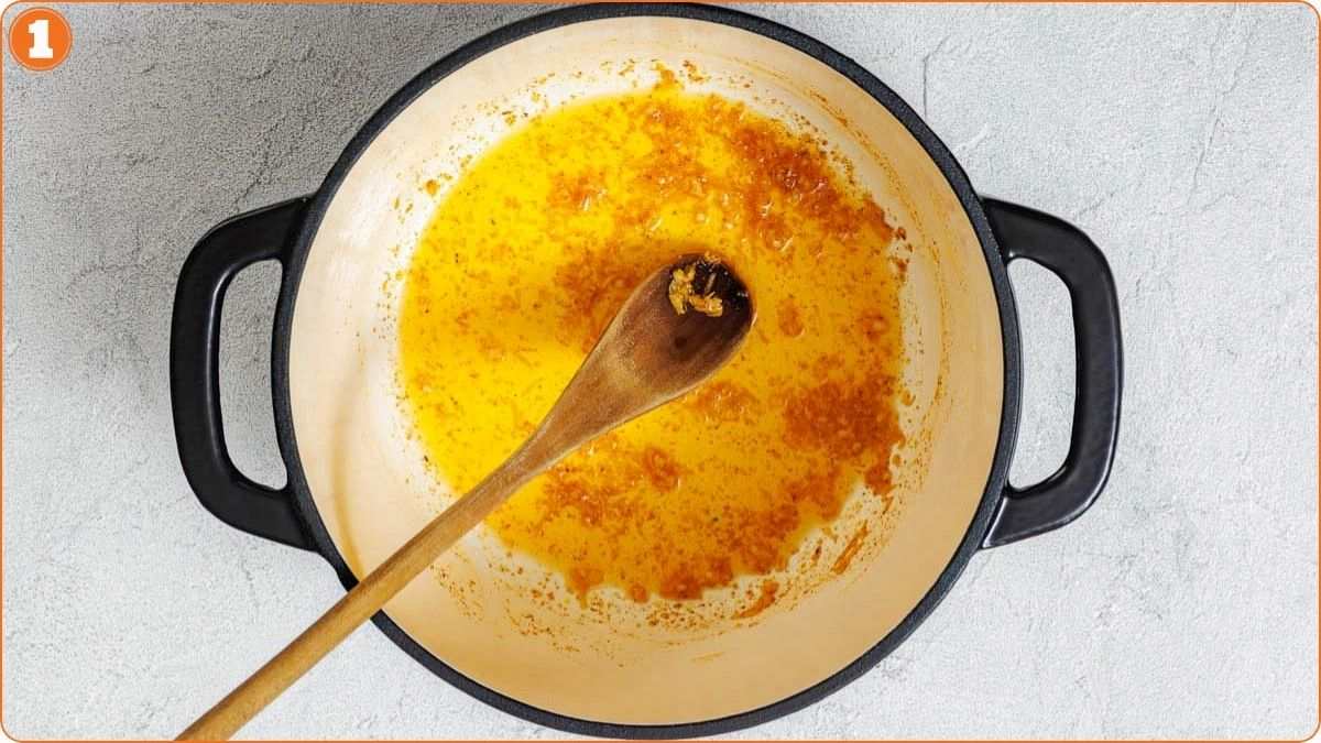 A wooden spoon stirring sautéed onions and oil in a round black Dutch oven on a light countertop.