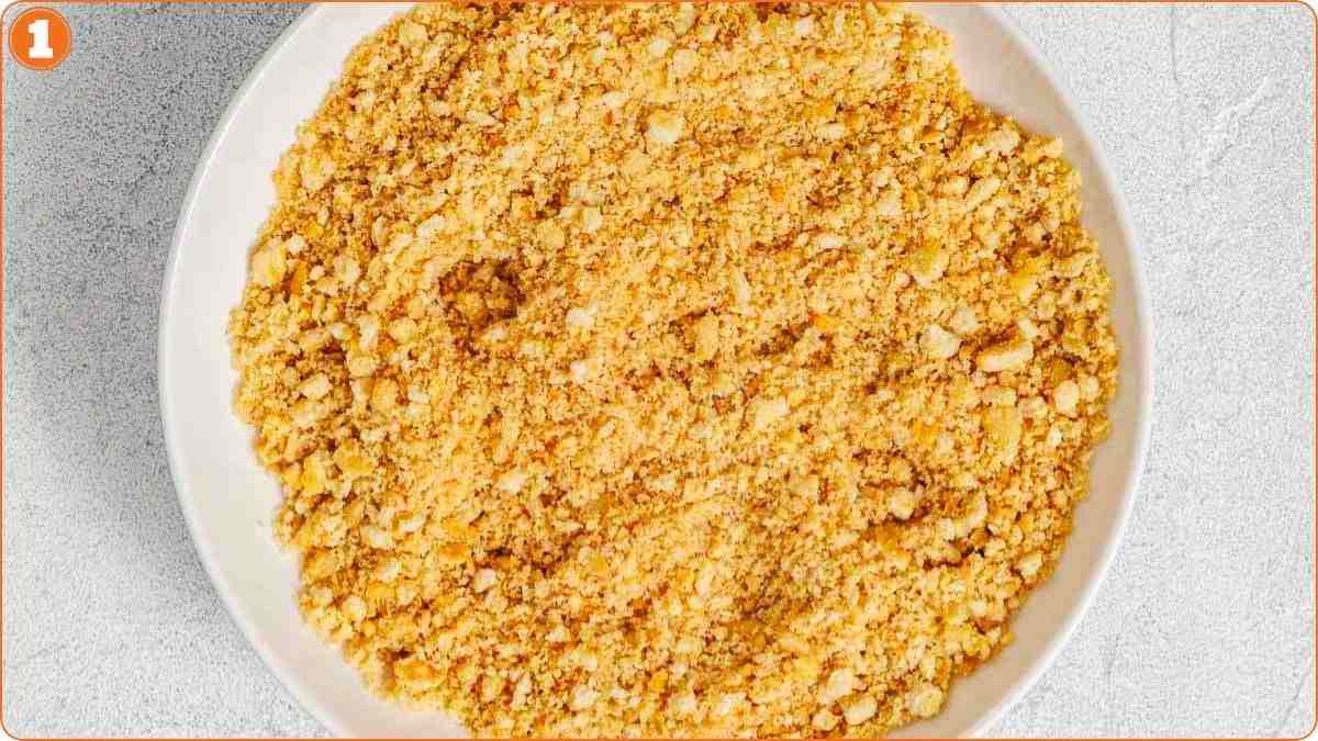 A white bowl filled with finely crushed golden-brown crumbs, placed on a light gray surface.