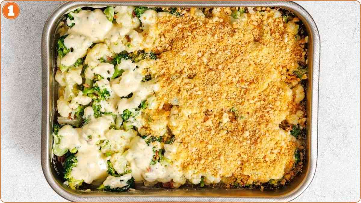 A casserole dish filled with broccoli and cauliflower covered in creamy sauce, half topped with a layer of golden breadcrumbs.