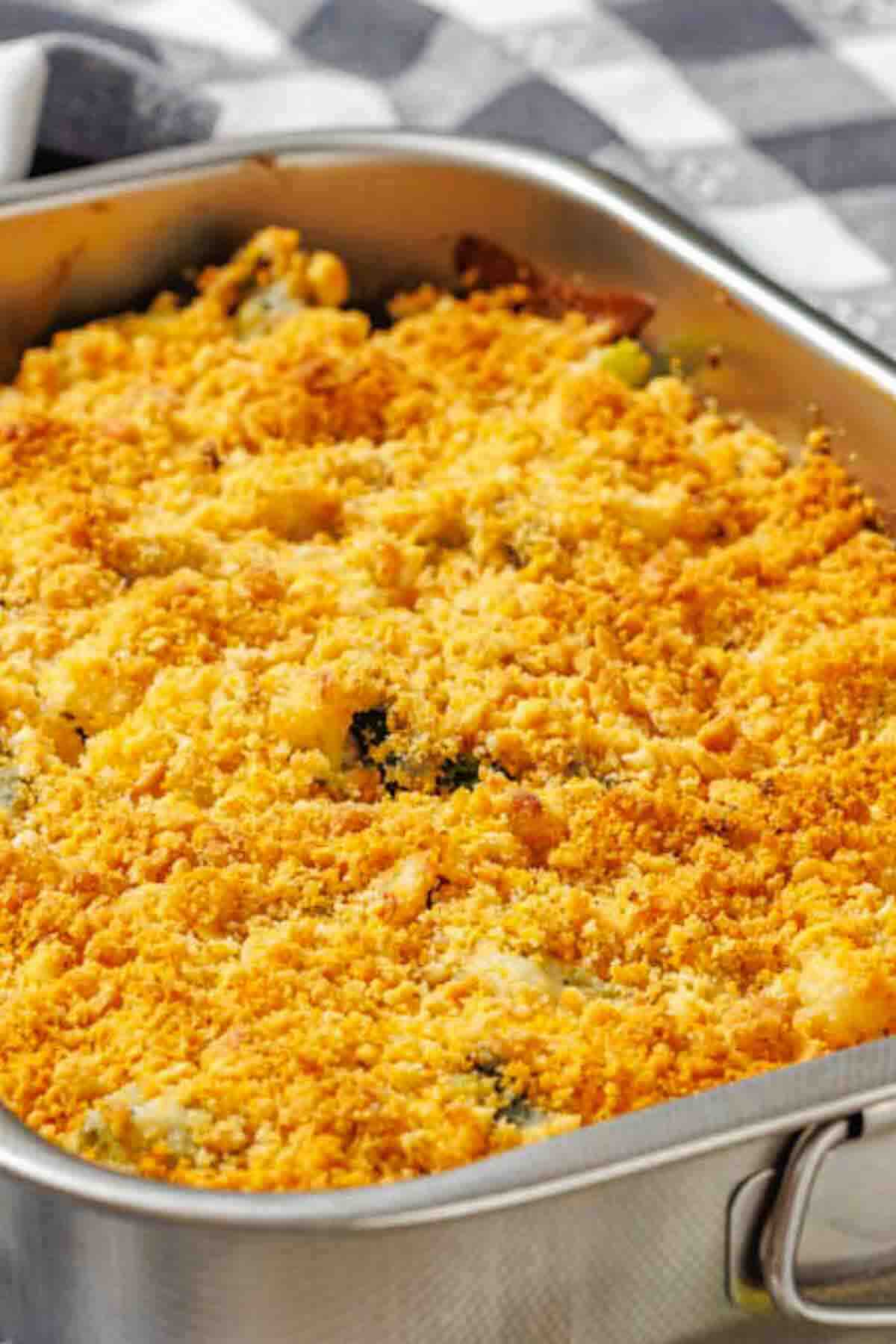 A baked casserole topped with a golden, crispy breadcrumb crust in a stainless steel pan on a checkered tablecloth.