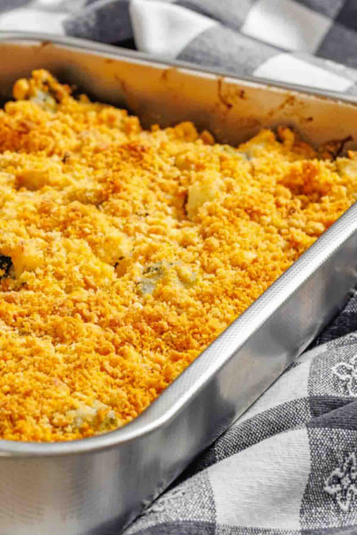 A close-up of a baked casserole with a golden, crumbly topping in a rectangular metal pan on a checkered cloth.