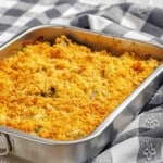 A rectangular metal baking dish filled with a casserole topped with a golden, crumbly crust, set on a patterned cloth.