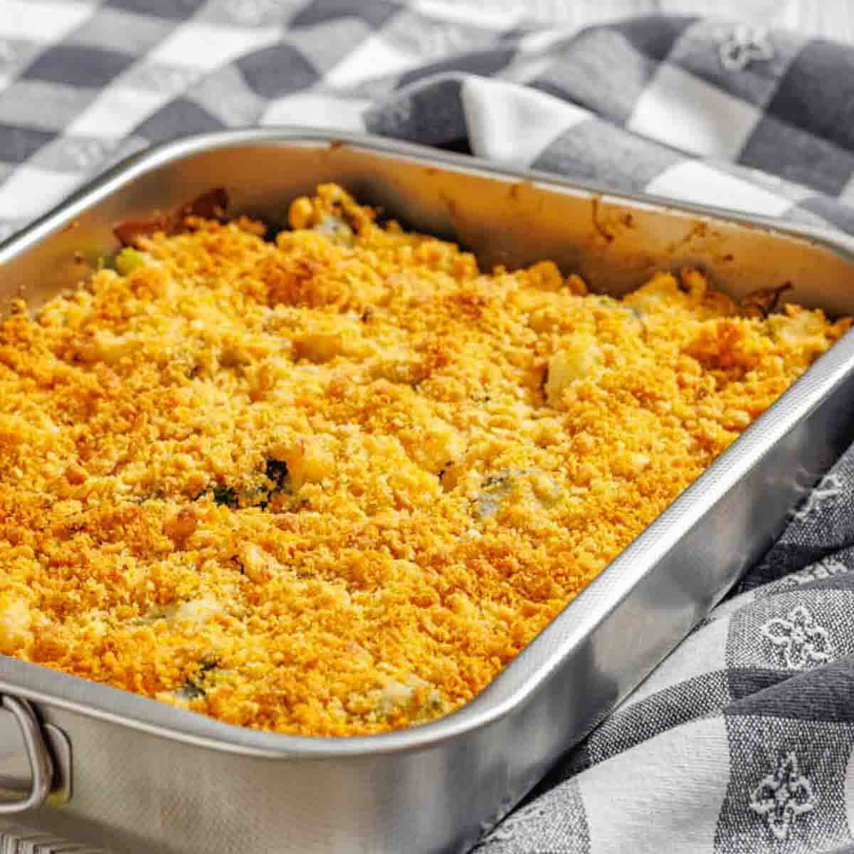 A rectangular metal baking dish filled with a casserole topped with a golden, crumbly crust, set on a patterned cloth.