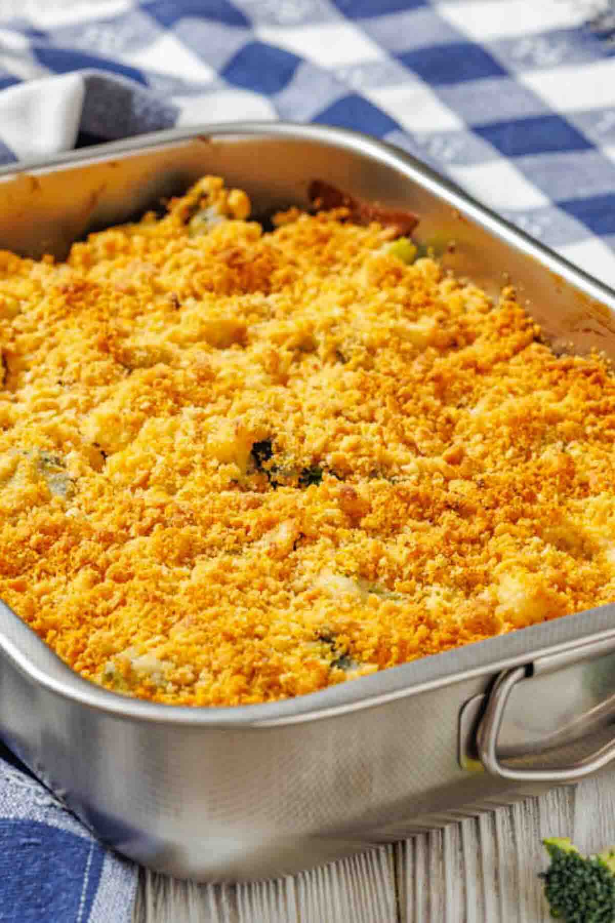 A rectangular metal baking dish filled with a golden-brown crumb-topped casserole sits on a blue and white checkered cloth.