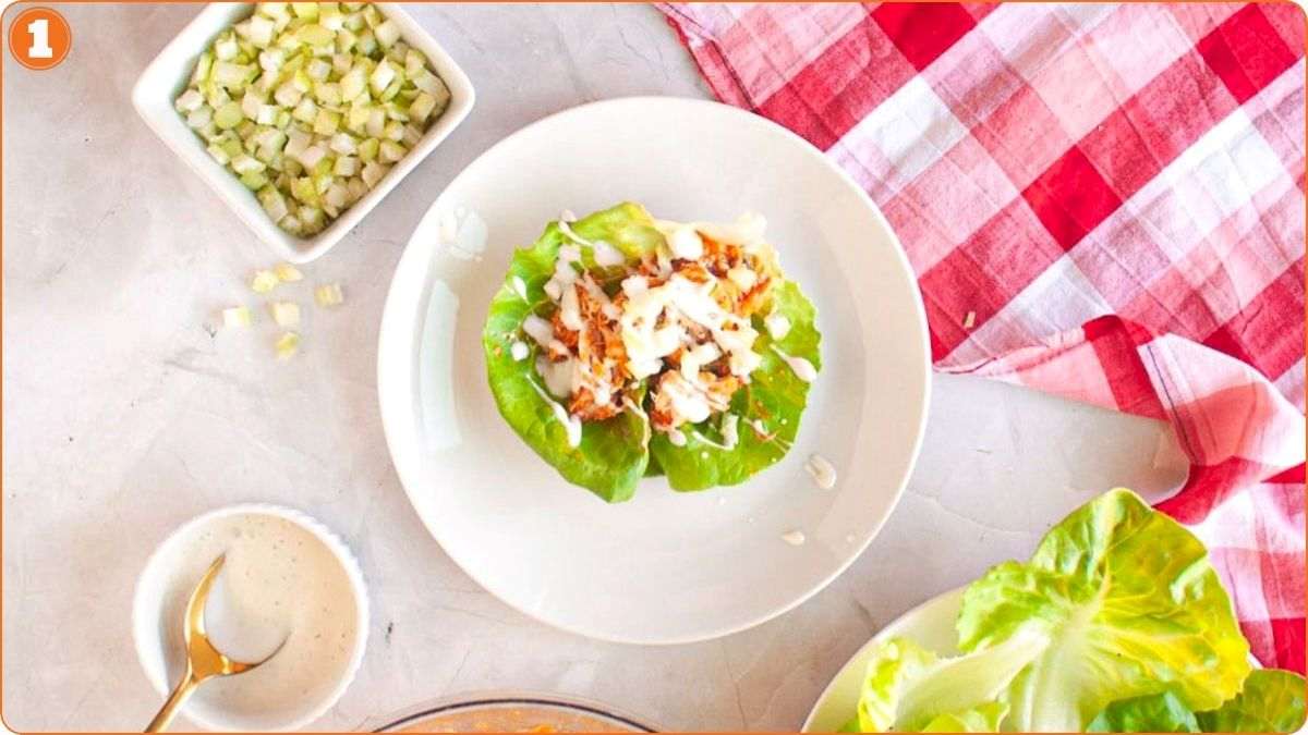 Assembling buffalo chicken lettuce wraps with dressing.