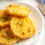 Close-up of several golden, breaded fried green tomato slices garnished with chopped herbs on a white plate.