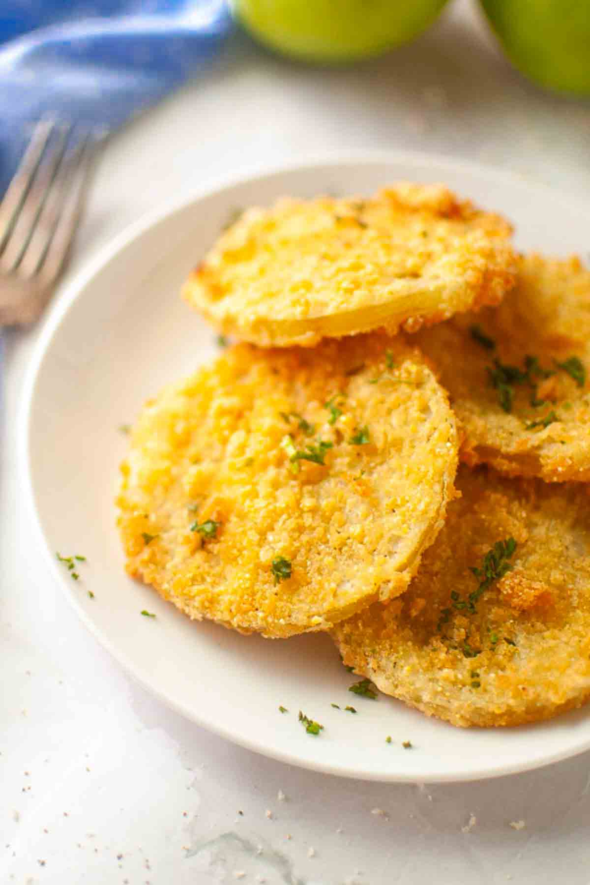 A white plate with several slices of breaded and fried green tomatoes, garnished with chopped herbs.