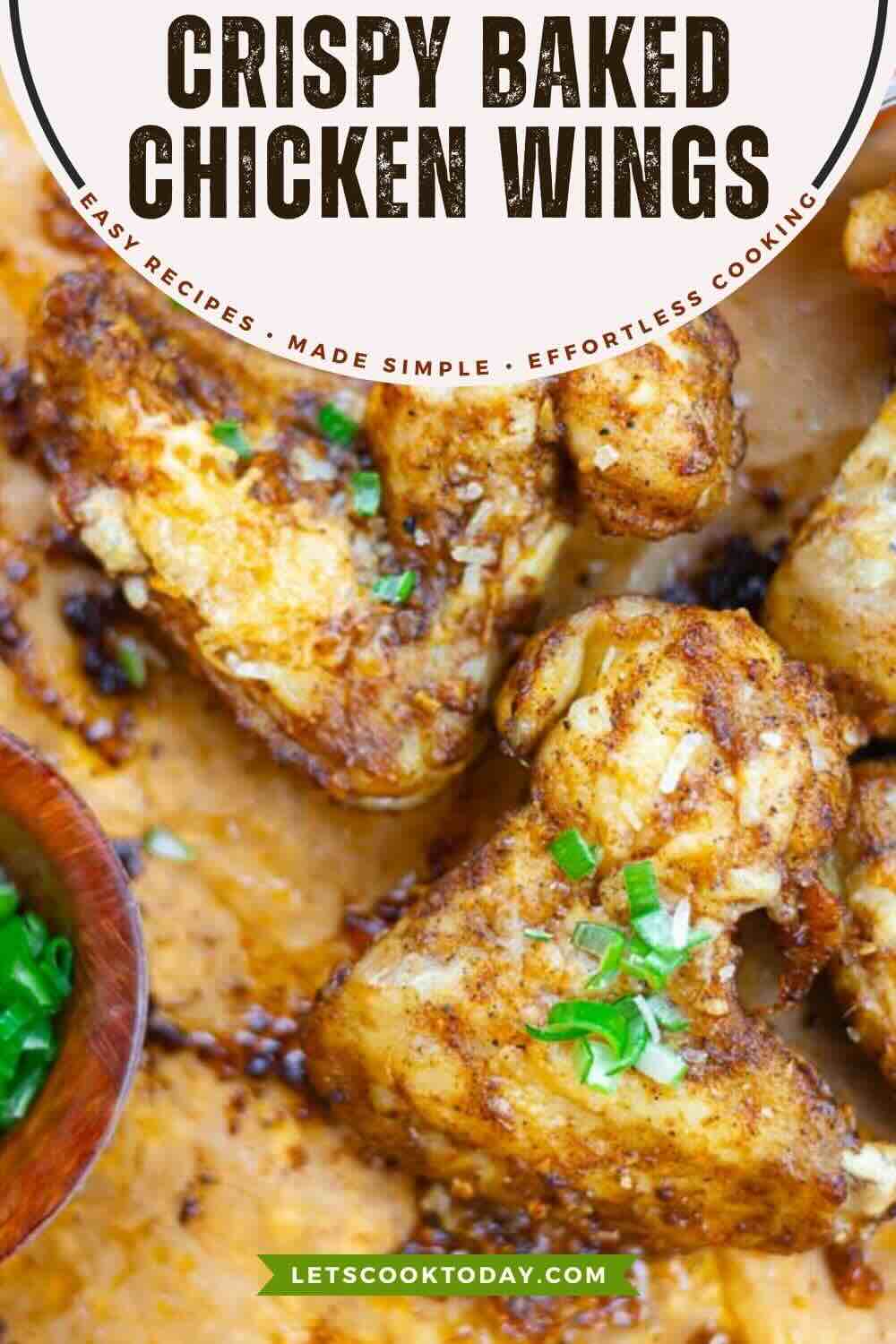 Close-up of crispy baked chicken wings garnished with chopped green onions on a parchment-lined tray.