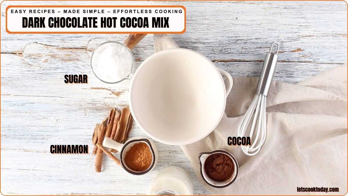 Top-down view of a bowl surrounded by labeled ingredients for dark chocolate hot cocoa mix: sugar, cinnamon sticks and powder, and cocoa powder, plus a whisk on a light wooden surface.