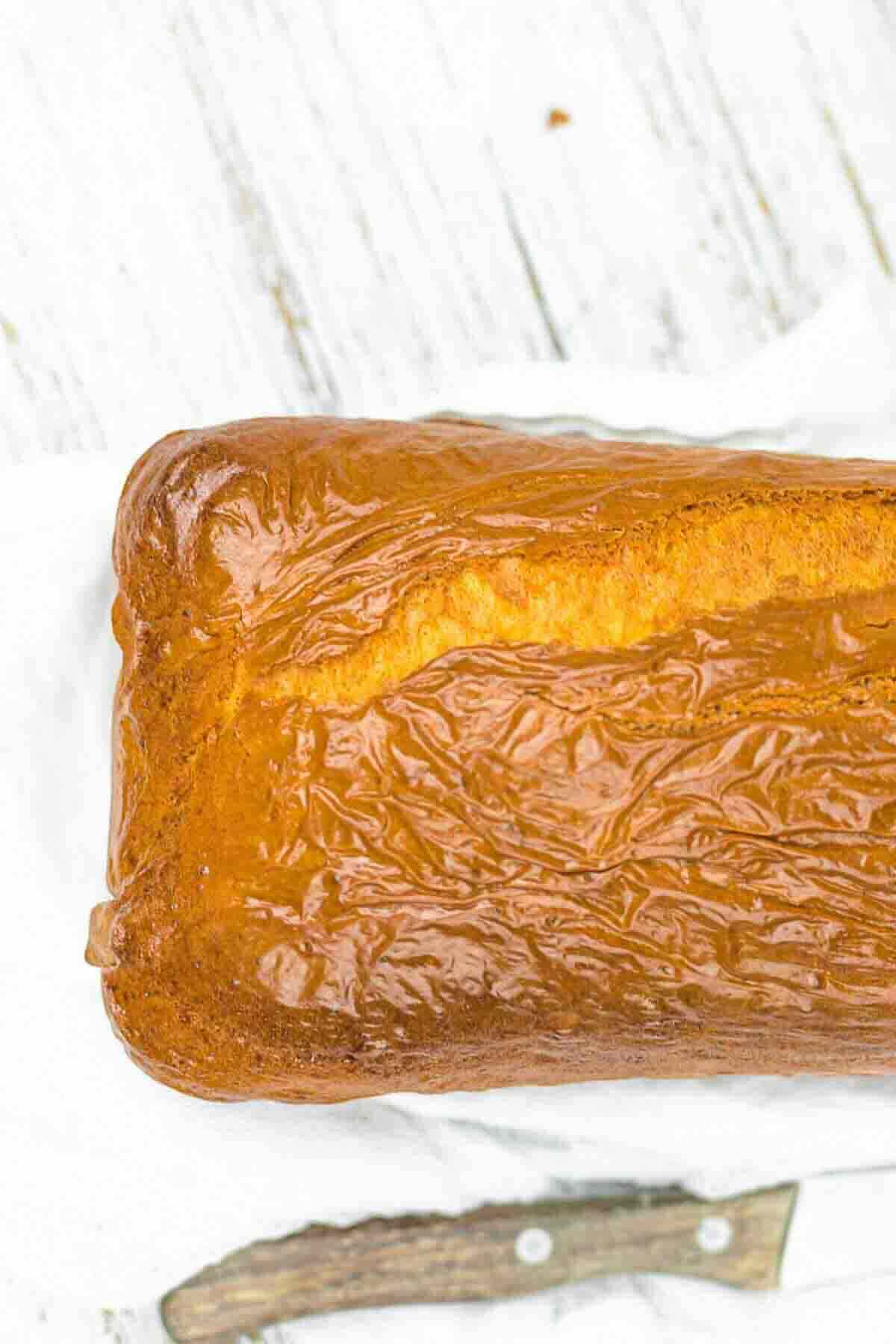 A close-up of a golden-brown loaf of bread resting on a white towel, with a wooden-handled knife partially visible underneath.