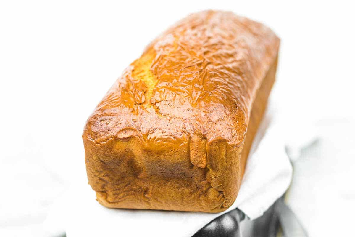 A loaf of golden-brown bread sits on a white cloth with a plain white background.