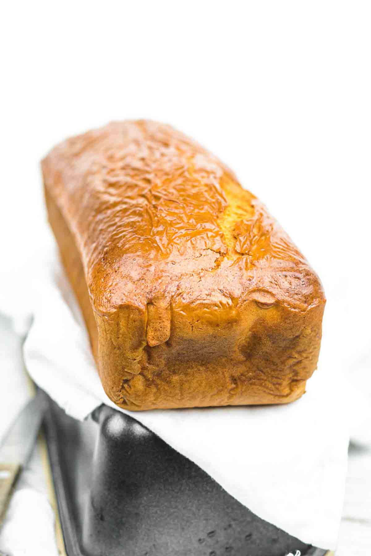 A loaf of golden-brown bread sits on parchment paper atop a black loaf pan against a white background.