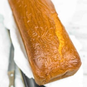 A loaf of freshly baked bread with a shiny, golden-brown crust rests on parchment paper next to a bread knife.