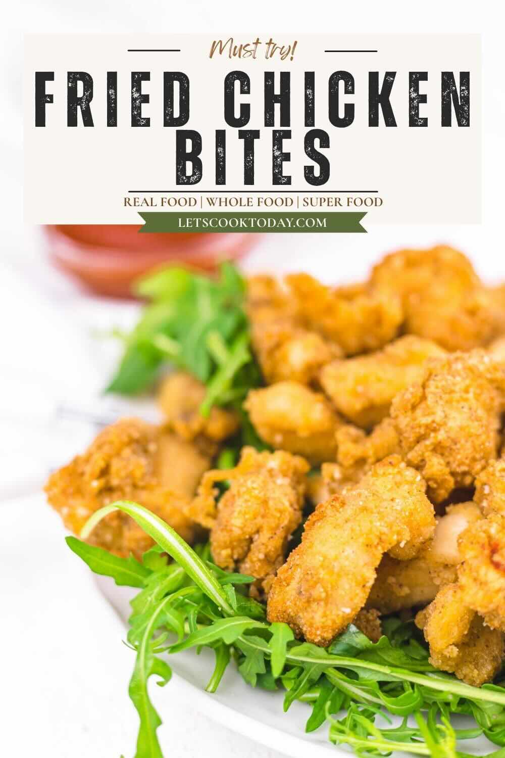 A plate of fried chicken bites on a bed of arugula with a side of dipping sauce, under a sign that reads "Fried Chicken Bites.