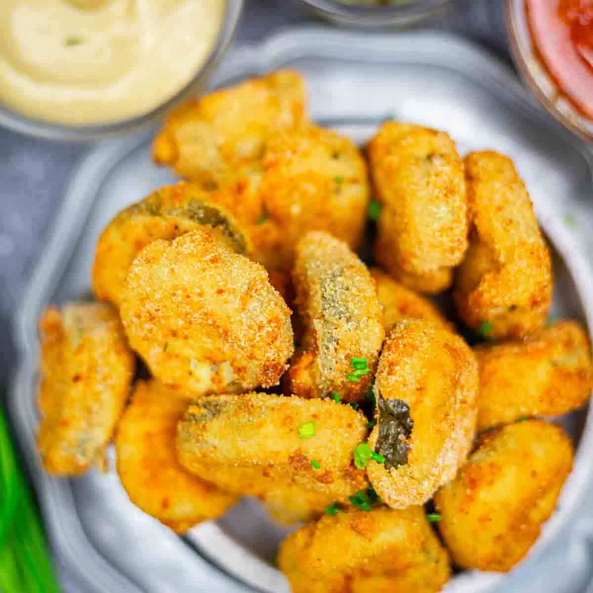 A plate of breaded and fried pickle chips is served with dipping sauces on the side.