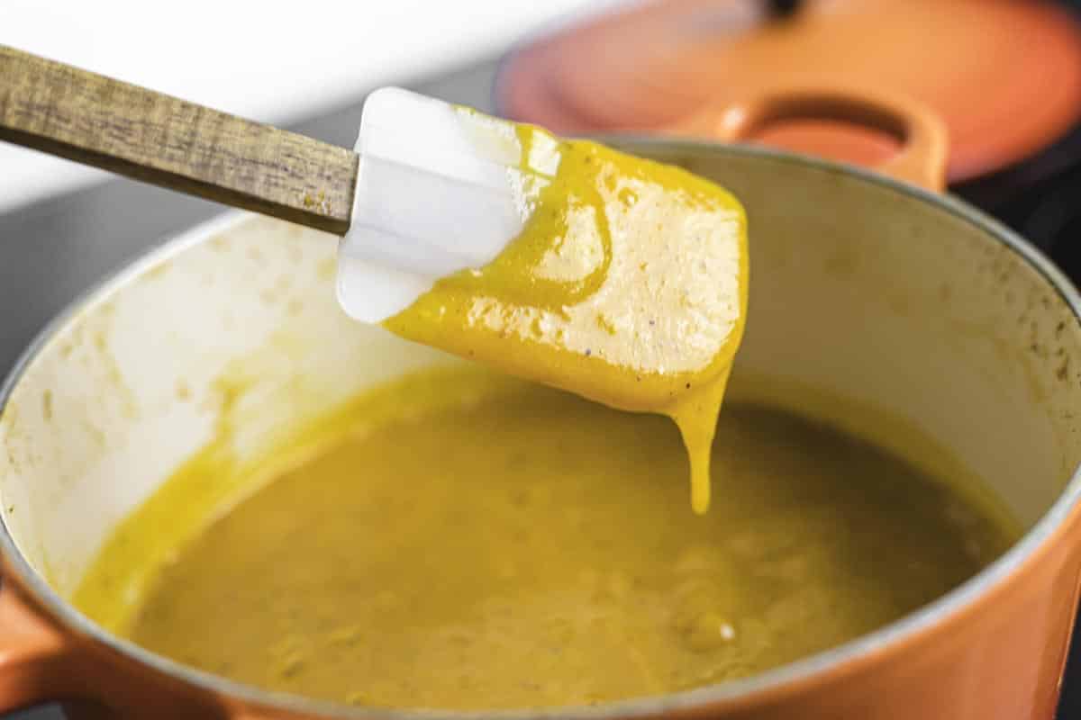 A white spatula with apricot sauce is held above a matching orange pot filled with the same sauce.