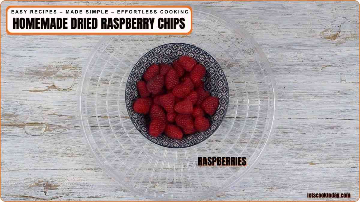 A bowl filled with fresh raspberries sits inside a larger clear bowl on a light wooden surface, with text labeling them as raspberries.