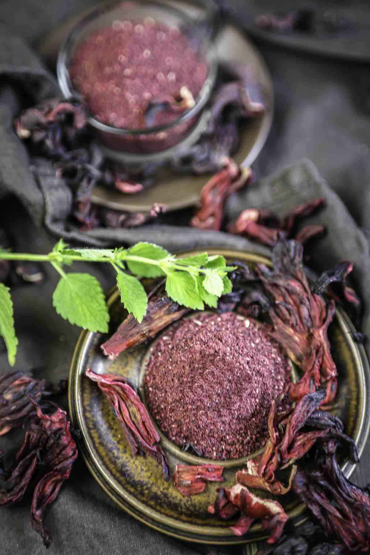 Bowl of powdered hibiscus surrounded by petals.
