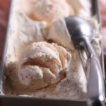 Container of strawberry ice cream with scoop.