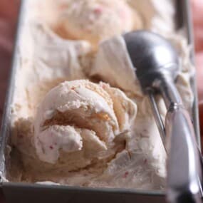 Container of strawberry ice cream with scoop.