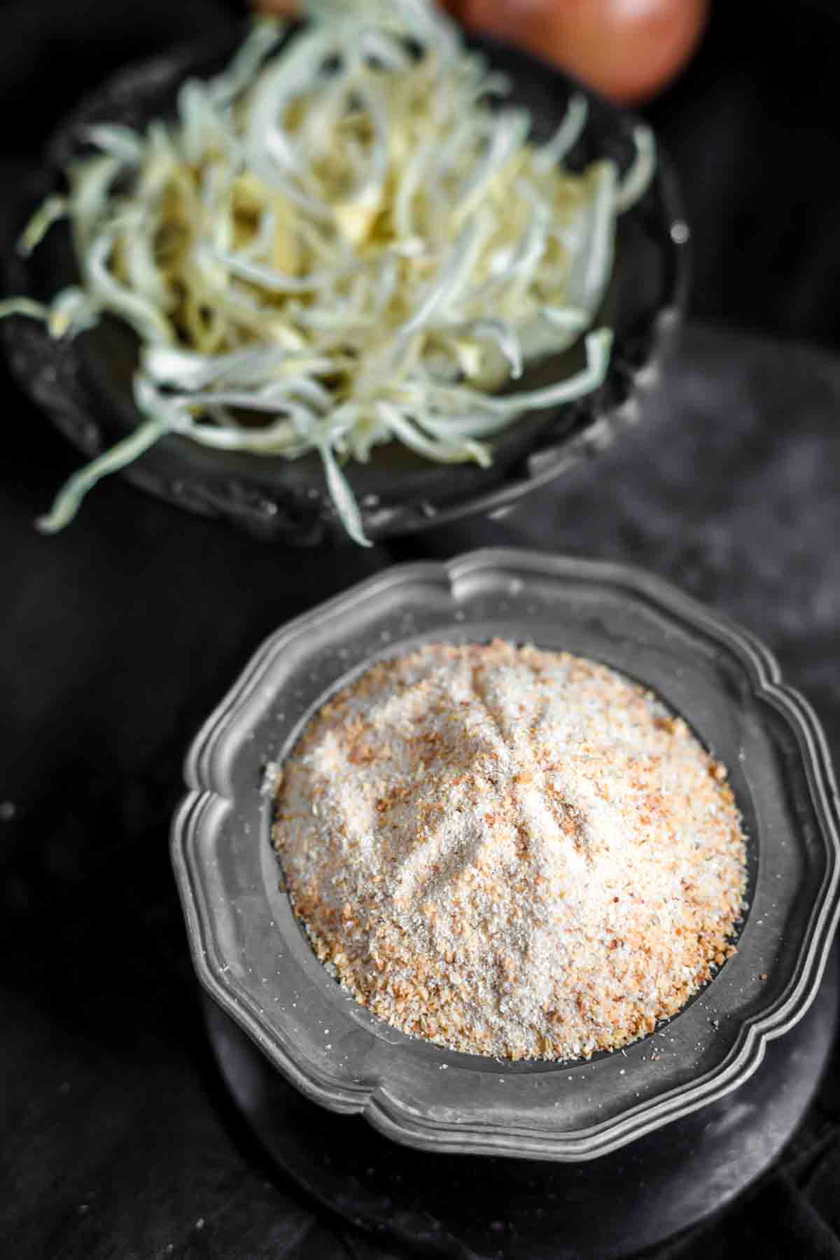 A bowl of finely ground powder sits in the foreground, with sliced dried onions on a separate plate in the background.