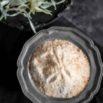 A black bowl filled with powdered seasoning sits next to a dish of shredded cabbage on a dark surface.