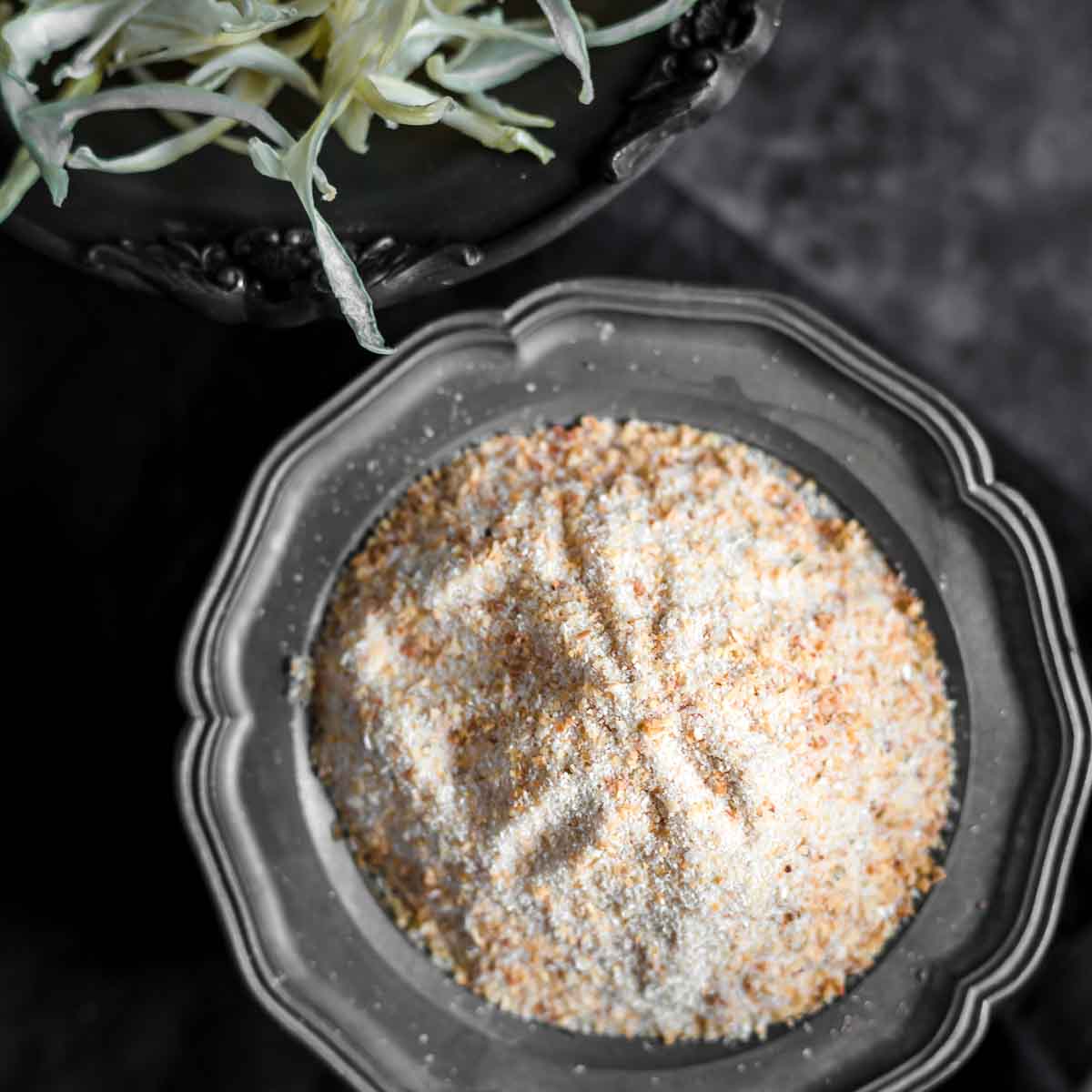 A black bowl filled with powdered seasoning sits next to a dish of shredded cabbage on a dark surface.