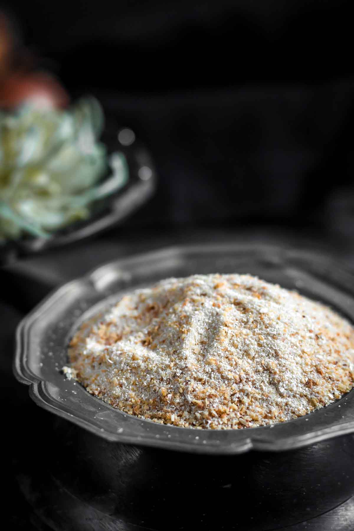 A close-up of a metal plate filled with a mound of breadcrumbs, with a blurred background.