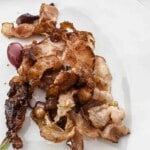 Crispy cooked bacon strips and red grapes on a white plate.