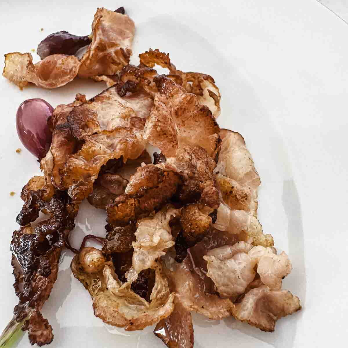 Crispy cooked bacon strips and red grapes on a white plate.