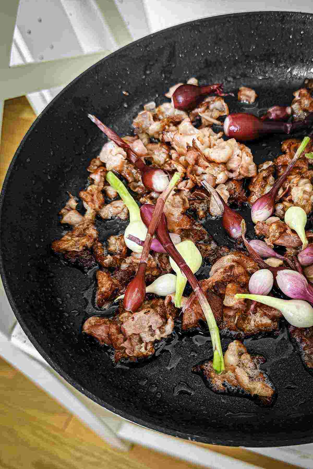Sliced bacon and whole spring onions cooking in a black frying pan.