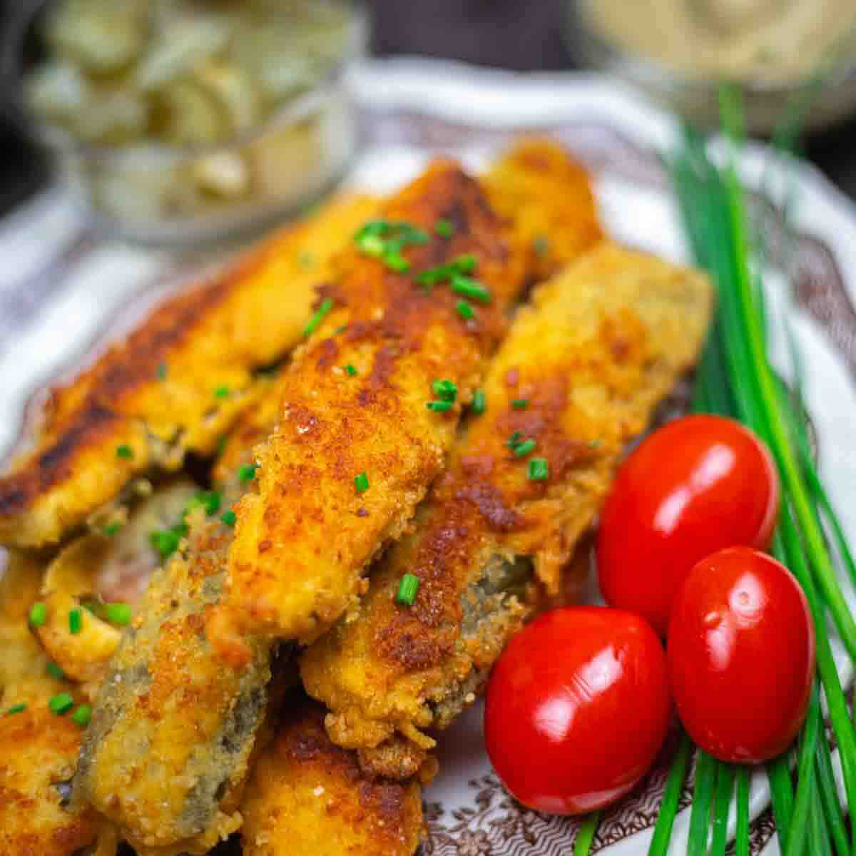 A plate of breaded and fried vegetable strips garnished with chopped chives, served with whole cherry tomatoes and fresh chives.