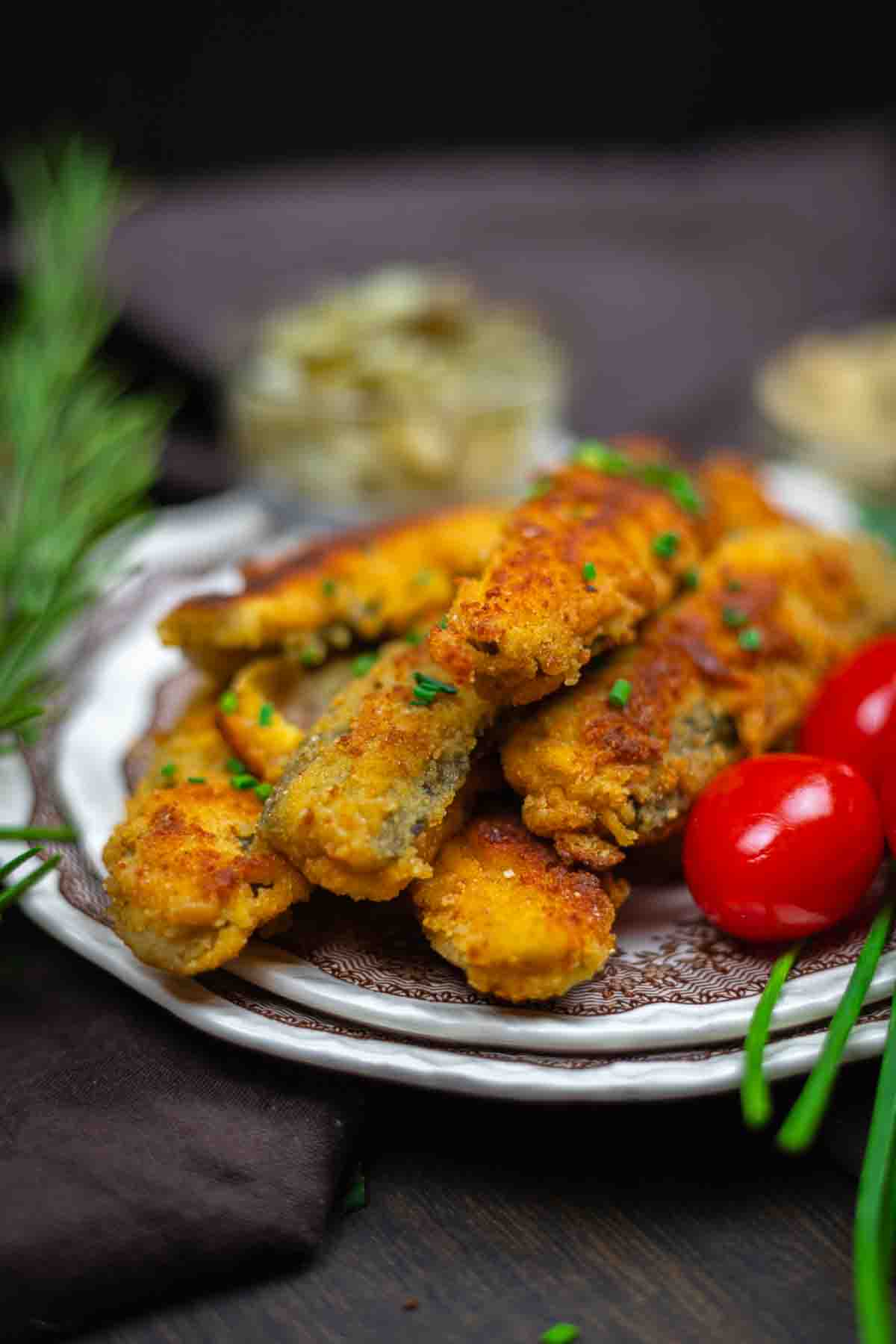 A plate of golden-brown breaded fried mushrooms garnished with chopped chives, served with cherry tomatoes and herbs.