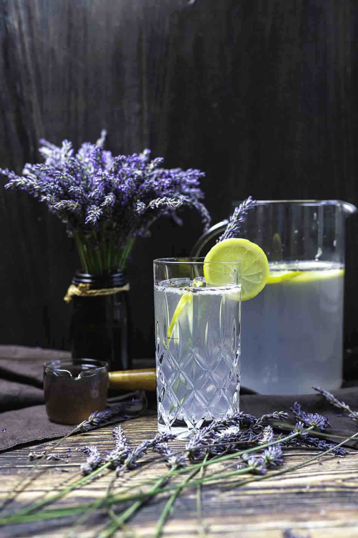 Glass of lavender mocktail beside fresh bouquet.