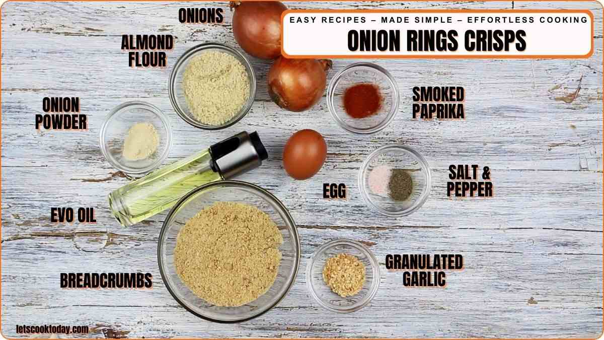 Top-down view of ingredients for onion rings crisps, including onions, almond flour, breadcrumbs, spices, egg, and oil, arranged on a wooden surface.