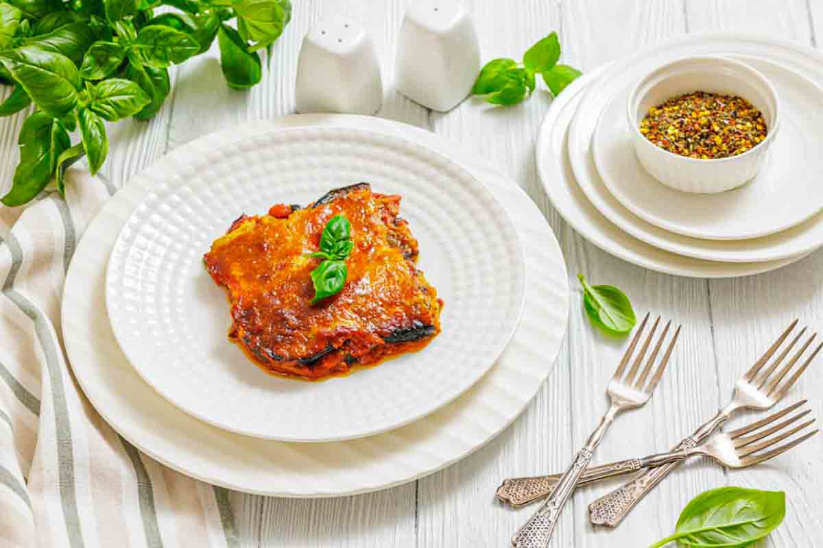 Eggplant parmesan on plate beside fresh basil.
