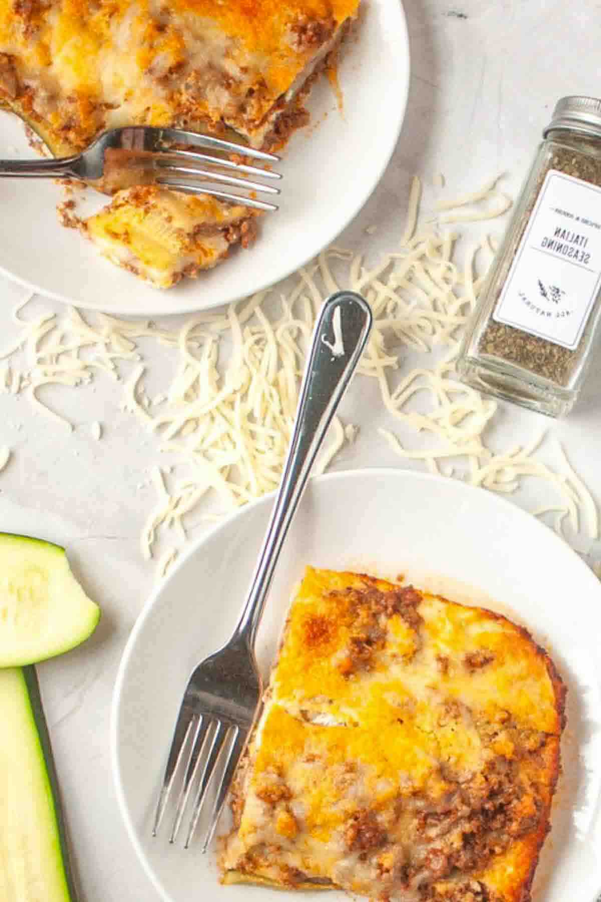 Two zucchini lasagna servings with Italian seasoning jar.