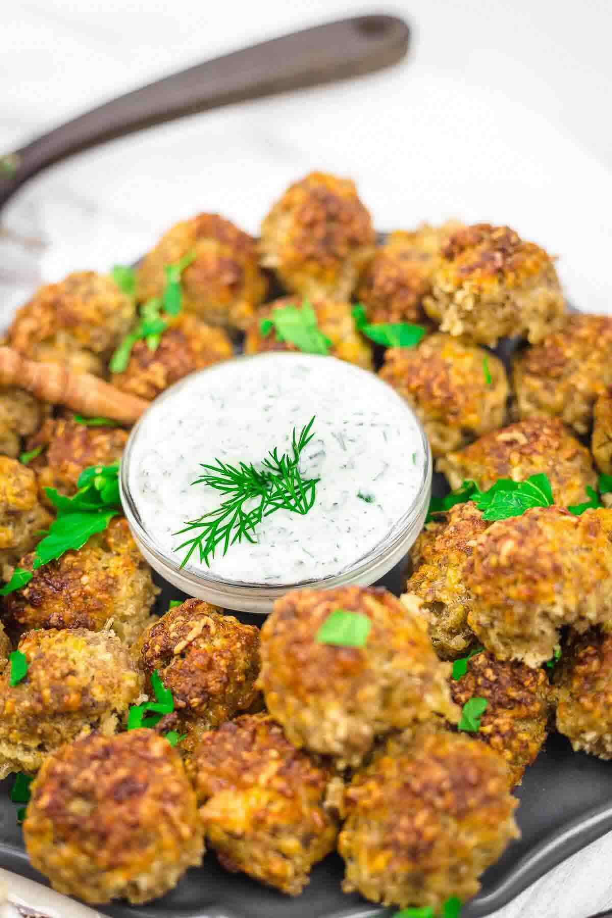 Crispy sausage balls beside bowl of dip.