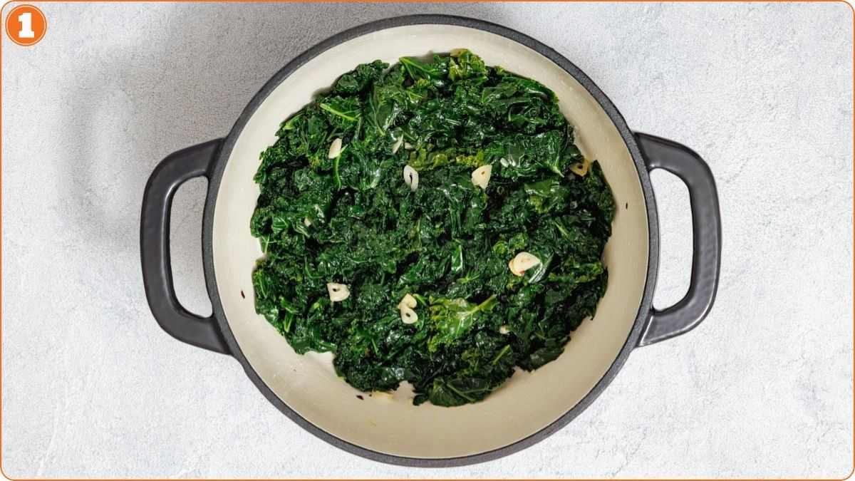 A pot of sautéed kale with sliced garlic pieces is shown from above on a light surface.