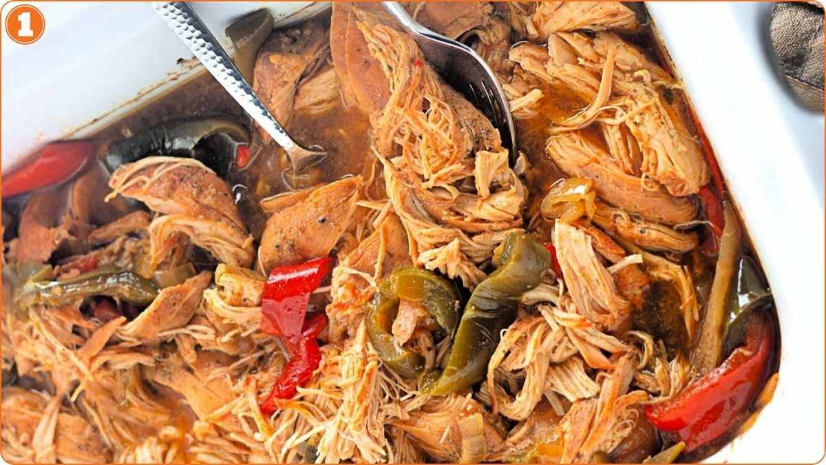 Shredded cooked meat with red and green bell peppers in a dish, with a serving spoon and fork.