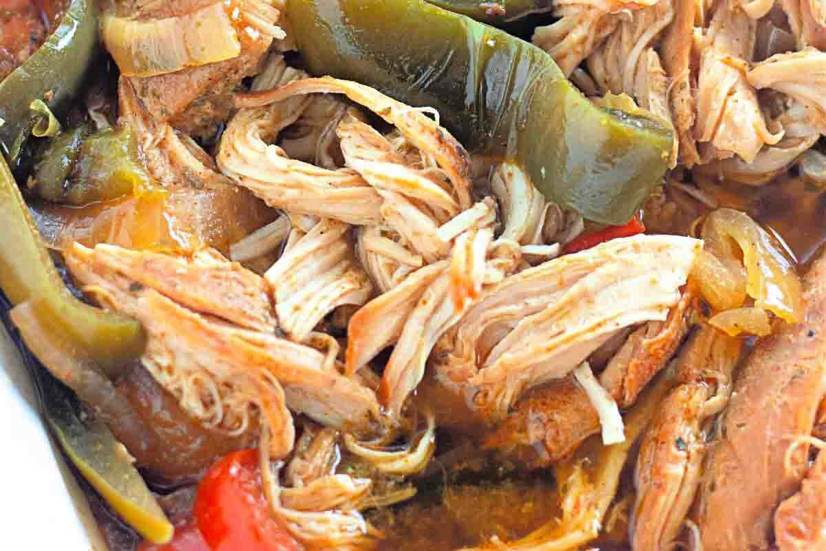 Close-up of shredded cooked chicken mixed with bell peppers and onions in a seasoned sauce.