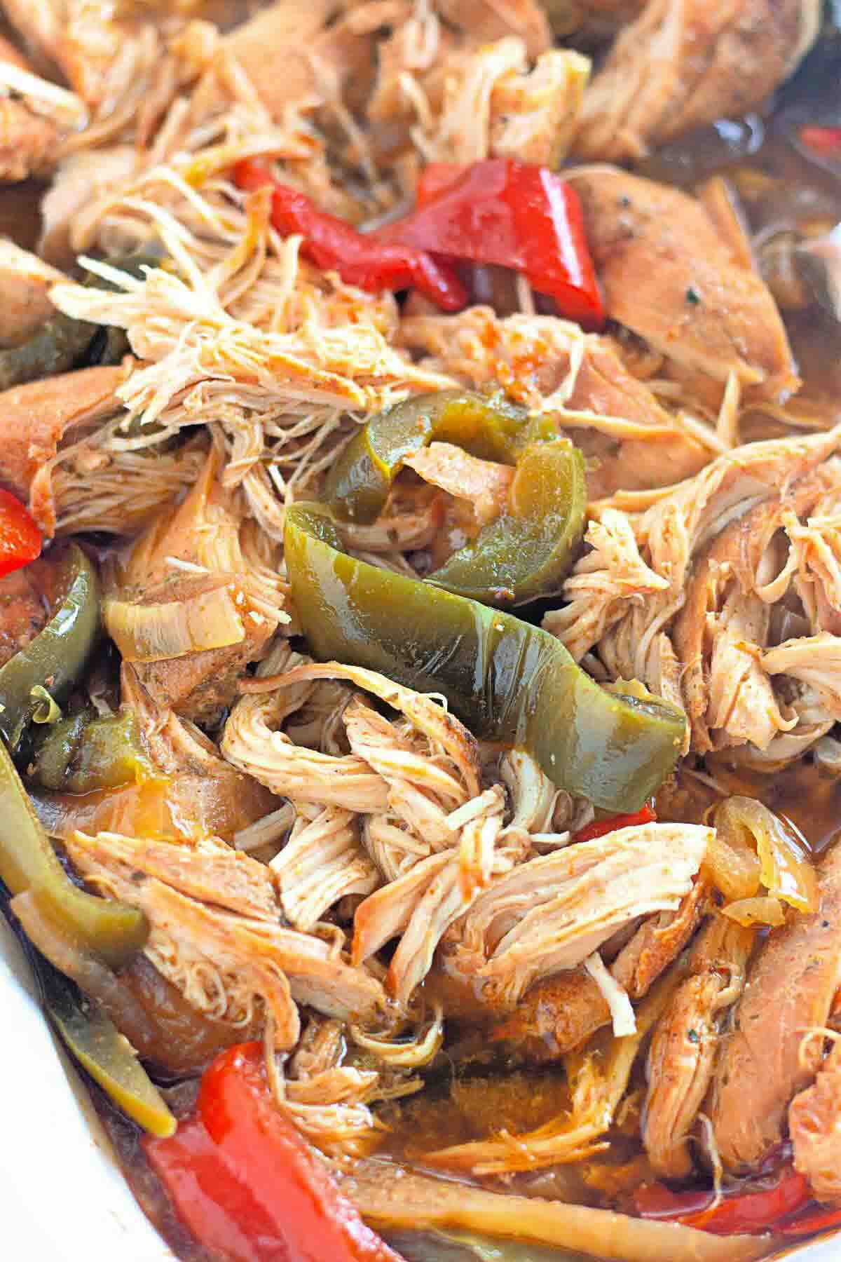 Close-up of shredded cooked chicken mixed with red and green bell pepper slices in a savory sauce.